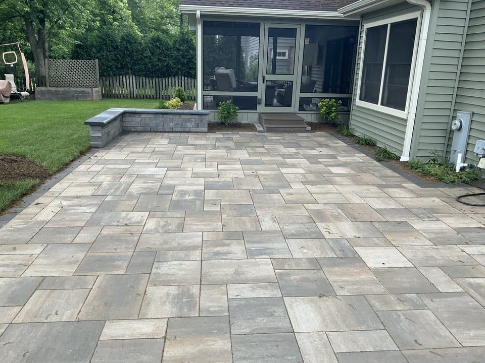 A Unilock paver patio with a seating wall and a stone fire feature at sunset.