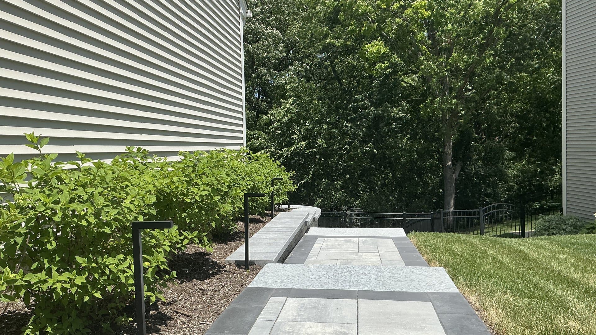 A lush front yard with crisp edging, mature plantings, and a paver walkway at golden hour.