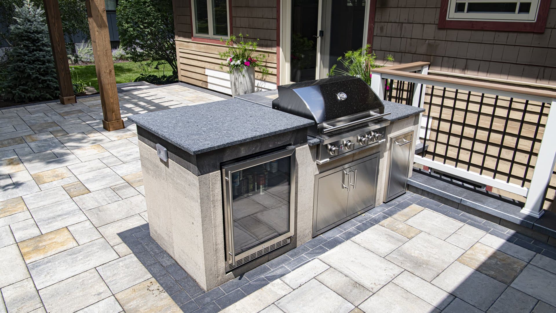 A paver patio with a stone fire feature at golden hour, surrounded by mature plantings.